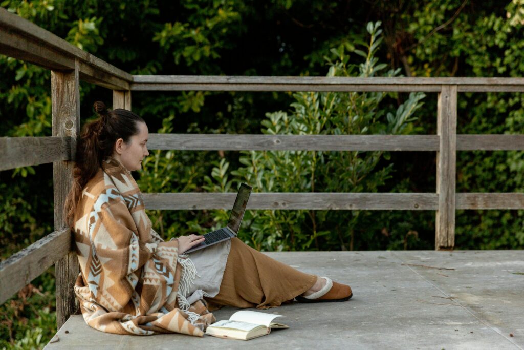 Adult focused female blogger sitting on veranda with laptop