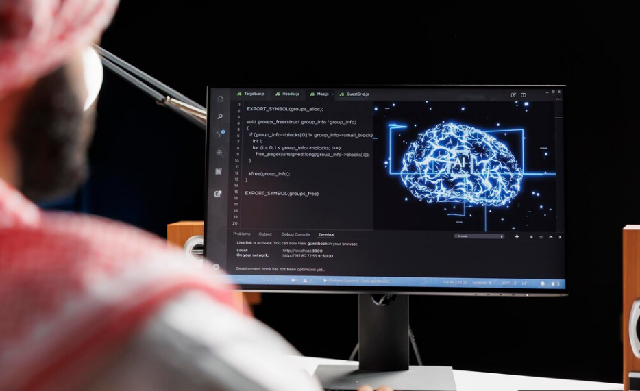 A blurred out person sitting in front of a dark mode computer screen the screen is filled with an image of computer programing code and what looks like a brain of AI connections.