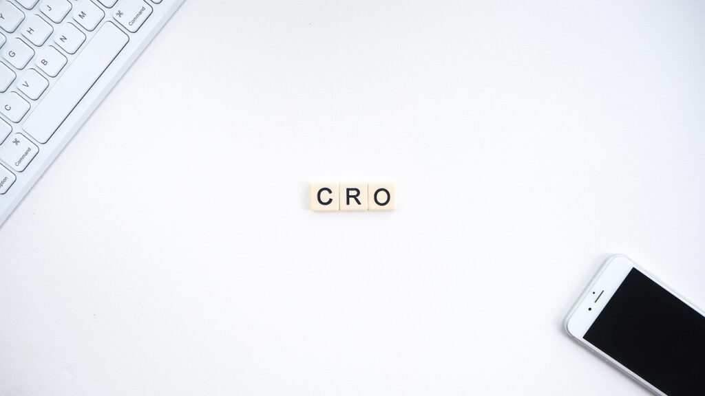 CRO on scrabble tiles in the middle of a white desk. A keyboard in one corner and a phone in the other.