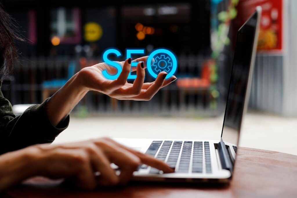 Woman's hand holding a neon SEO and working on her laptop with the other hand.
