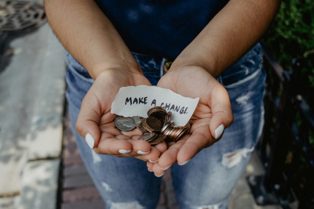 Two hands with palms face up holding onto a bunch of coins. There is a small torn piece of paper in the center that says "make a change".